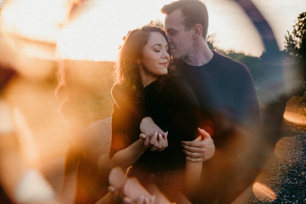 man kissing womans forehead as they sit in a field with light shining around them