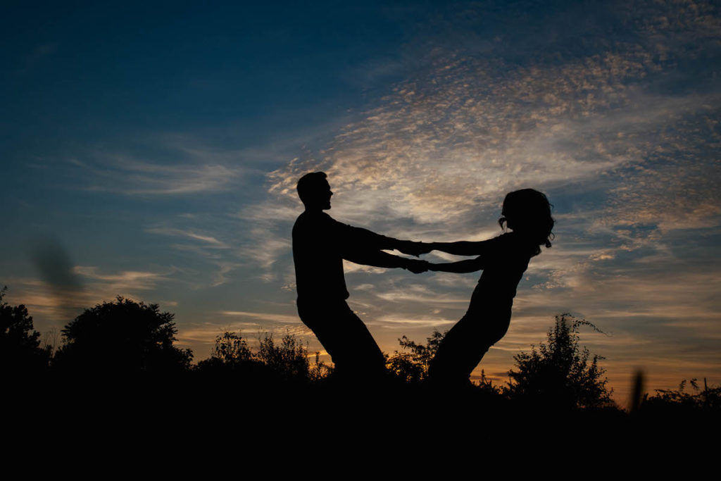 silhouette of two people holding hands and leaning back away from each other