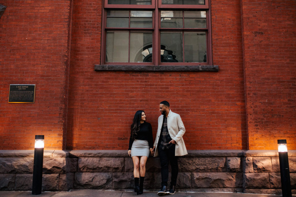 man and woman standing side by side looking at each other in front of a red brick building