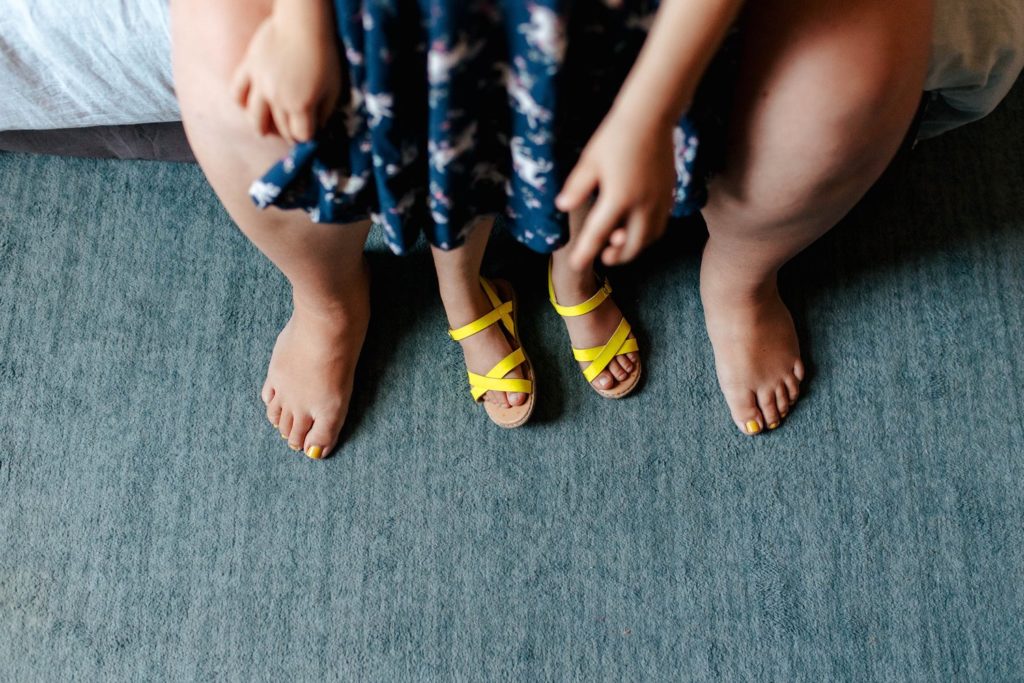 mother's feet with their daughter standing in between them wearing yellow sandals