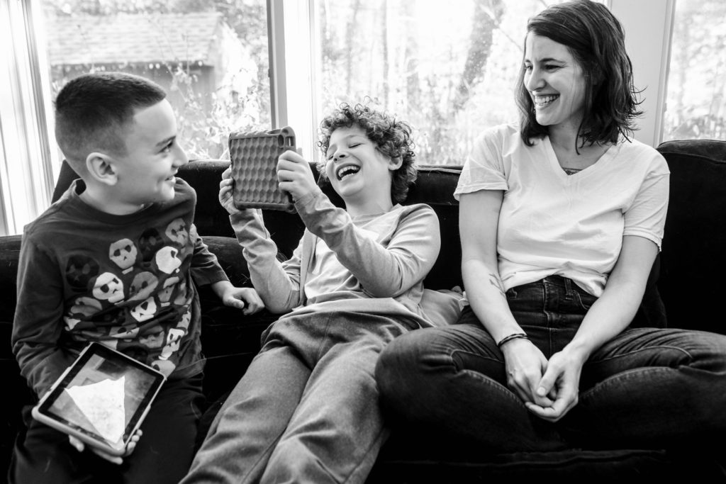 day in the life photography image of two sons sitting on a couch with their mother smiling and playin on tablets