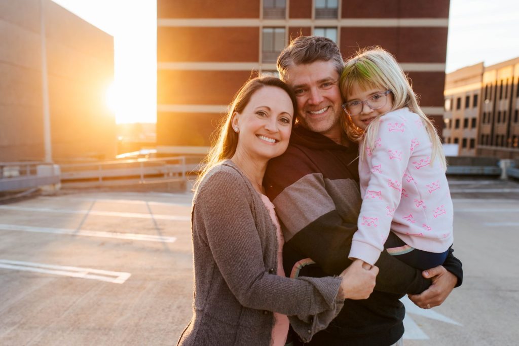 parents smiling together with their daughter in the father's arms at sunset