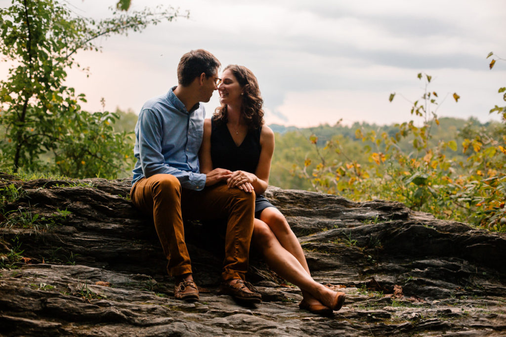man and woman sitting next to each other on a rock about to kiss