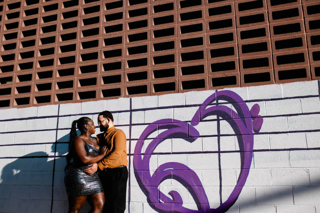 man and woman hugging each other while standing next to a mural on a city building