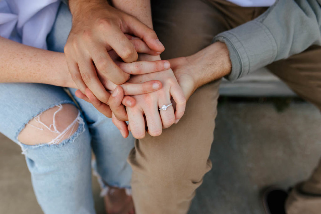 two sets of hands laid on top of legs showing off an engagement ring