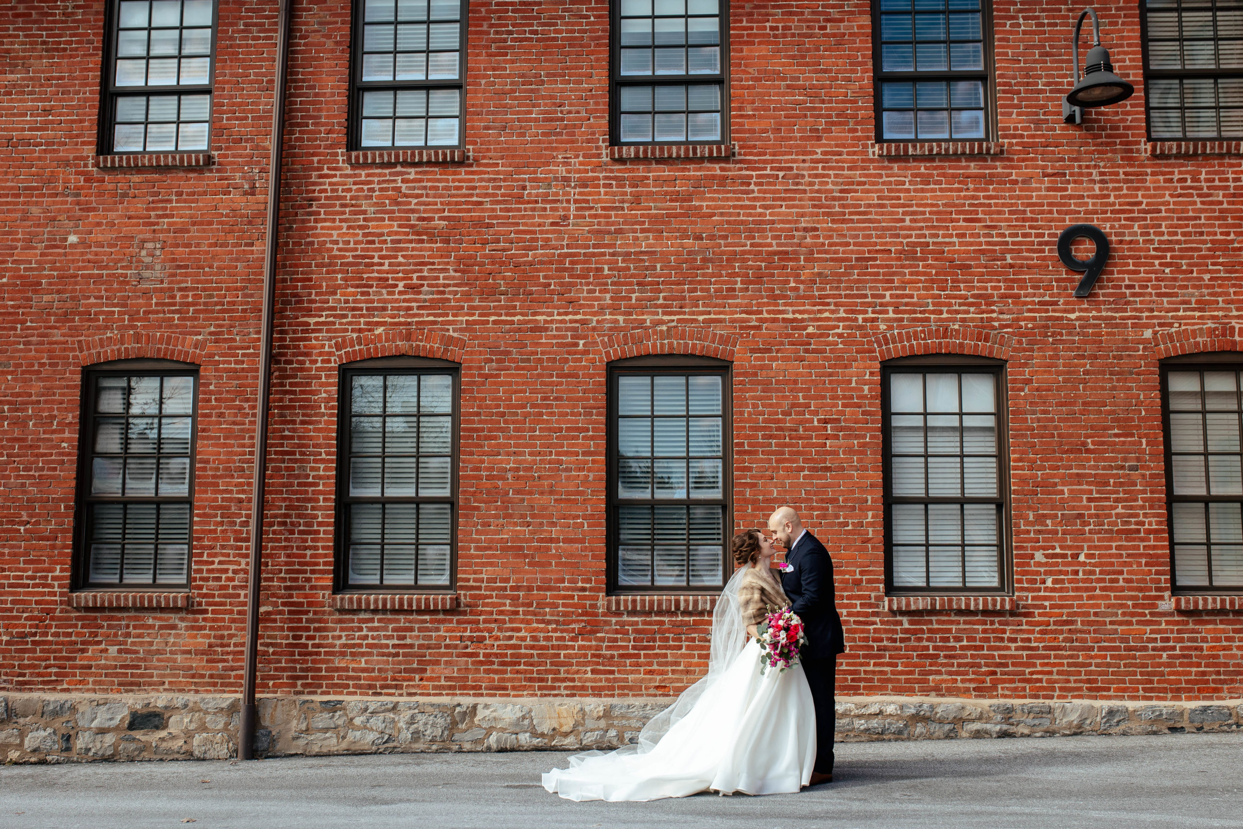 bride and groom kissing in front of a large brick building