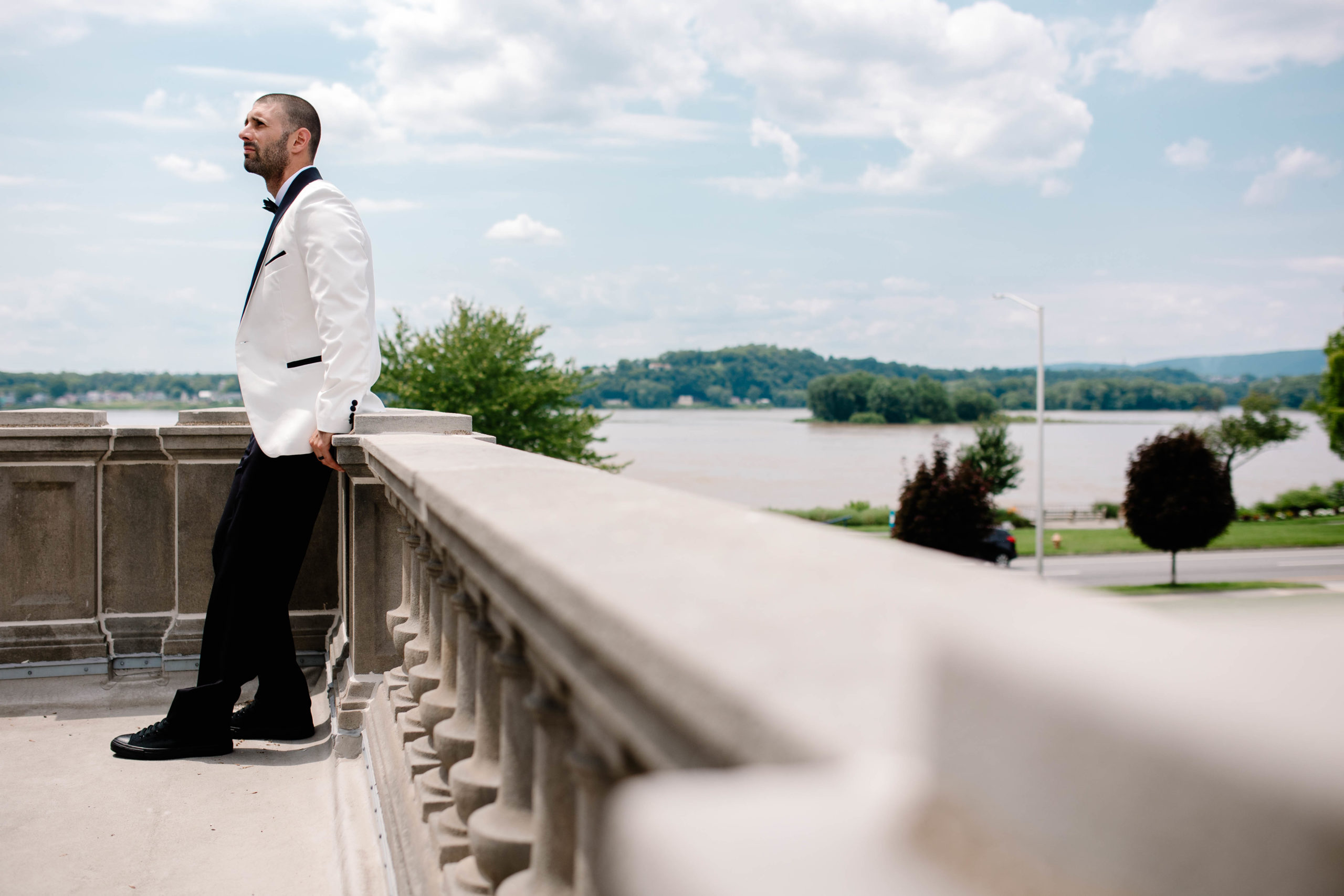 groom leaning against a white banister outside 