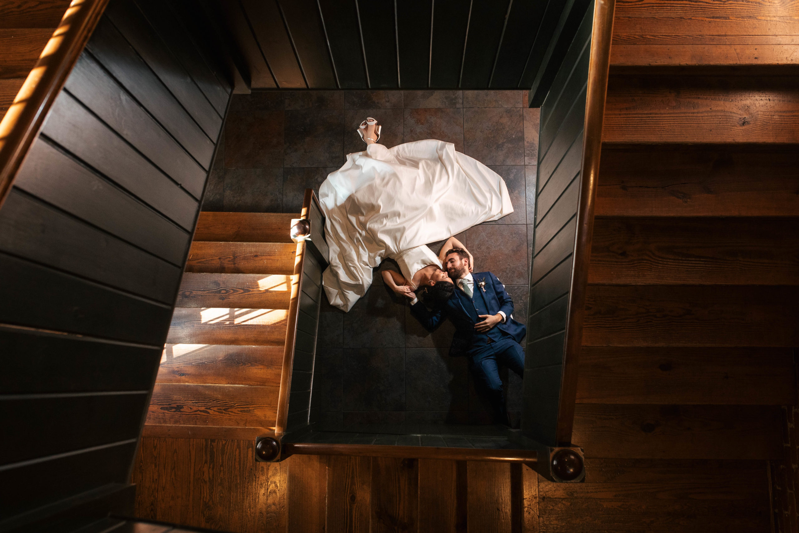 bride and groom laying together at the bottom of a square spiraled staircase 