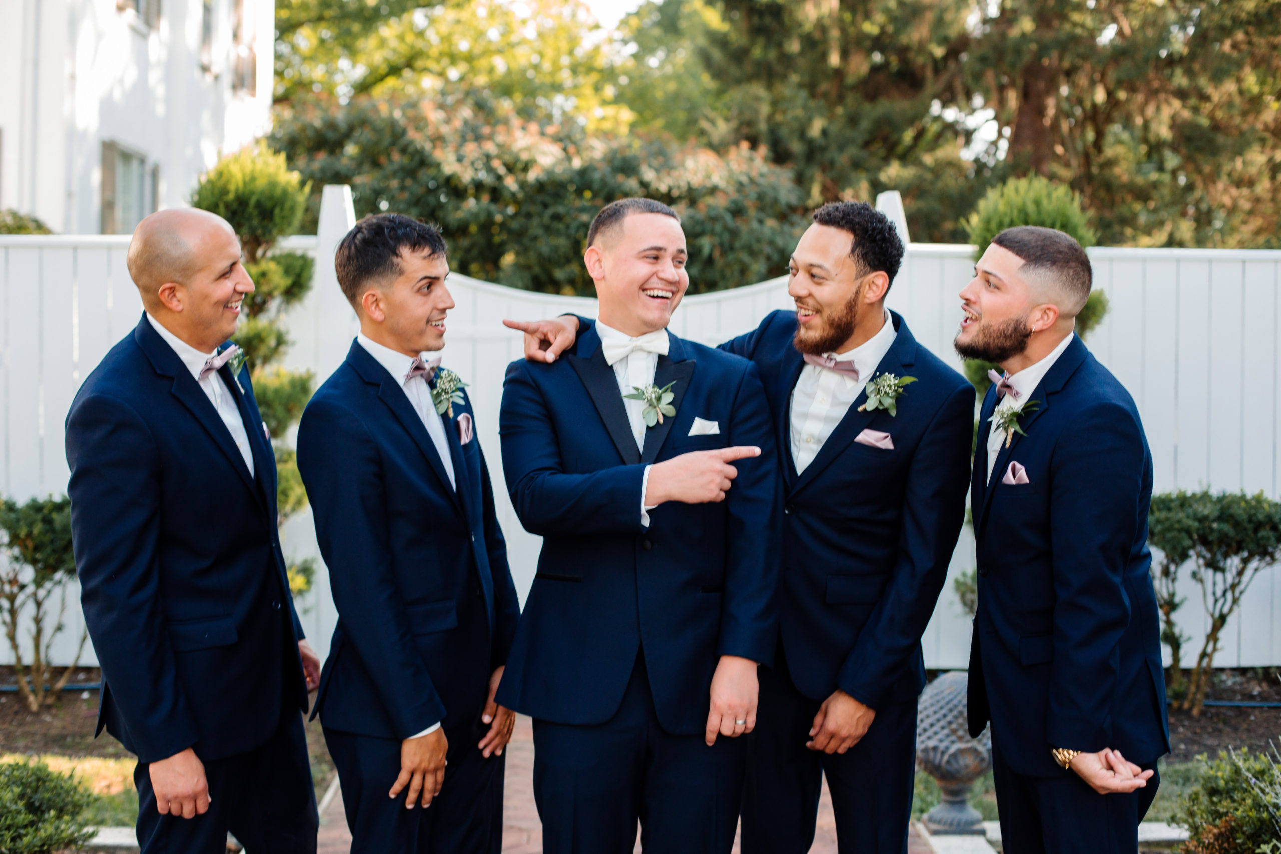 groom pointing towards one of his groomsman with other groomsmen standing around him