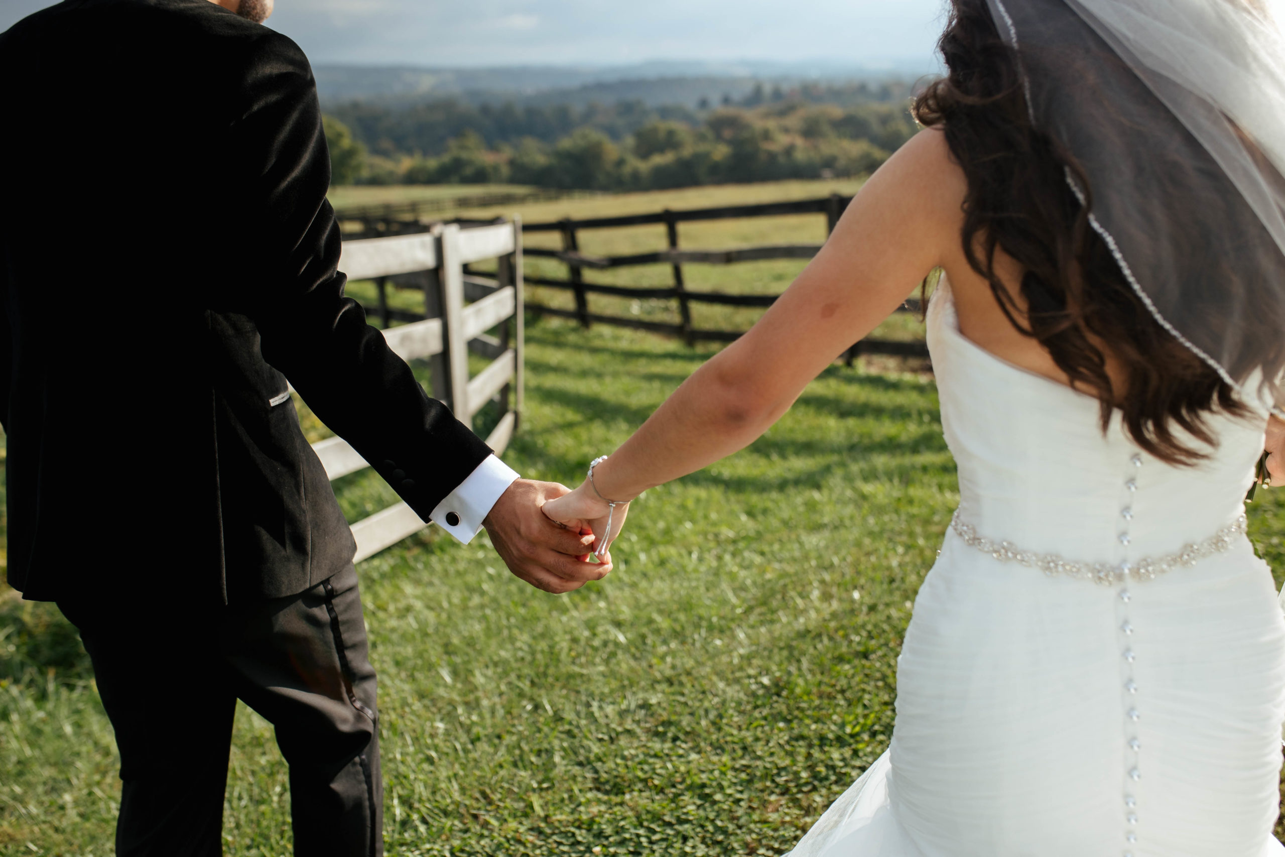 bride and groom holding hands walking through a field 