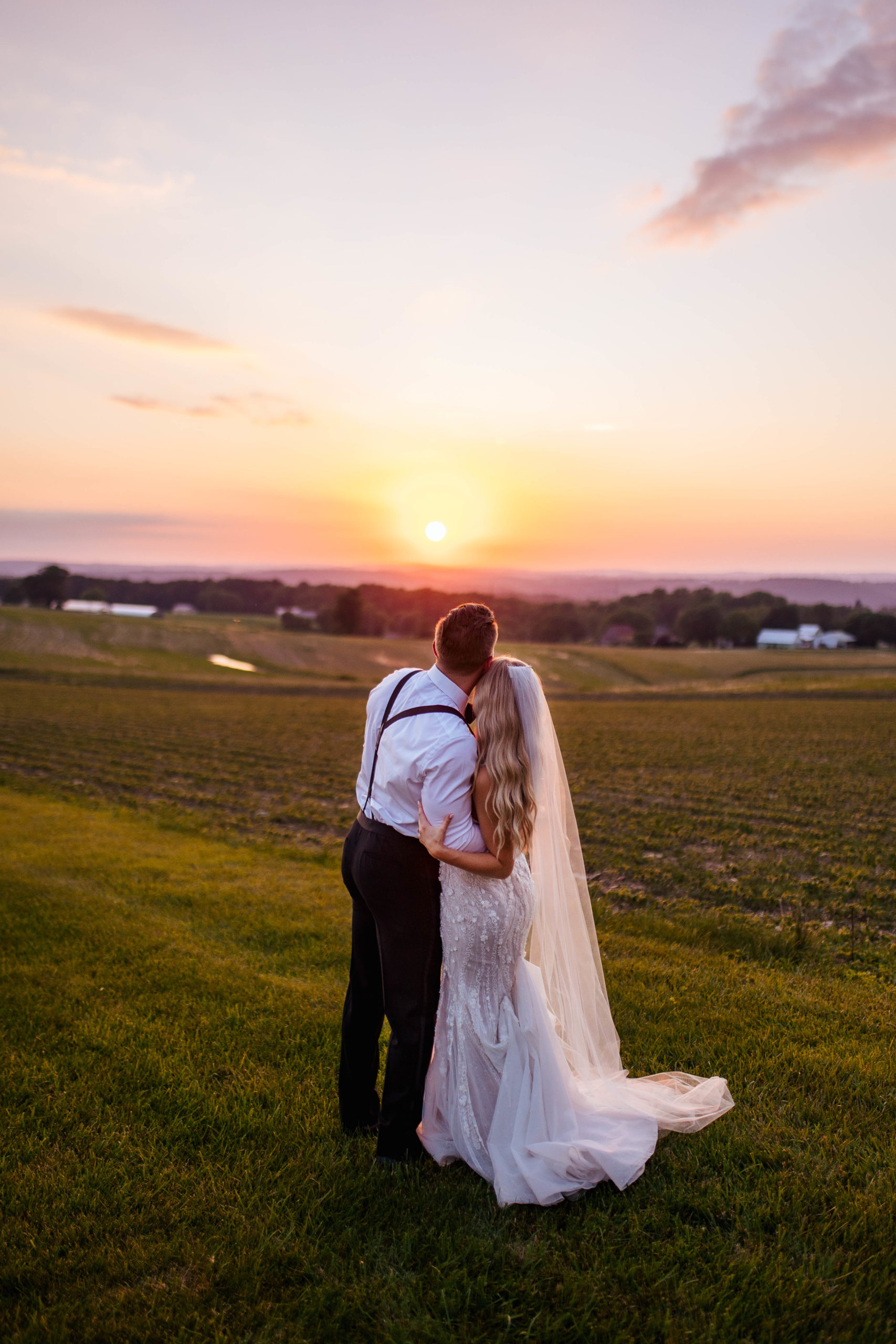 bride and groom hugging each other and watching the sunset in a large field